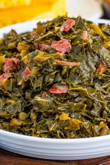 Bowl of Southern Collard Greens Recipe with shredded ham hocks served alongside cornbread and fried chicken.