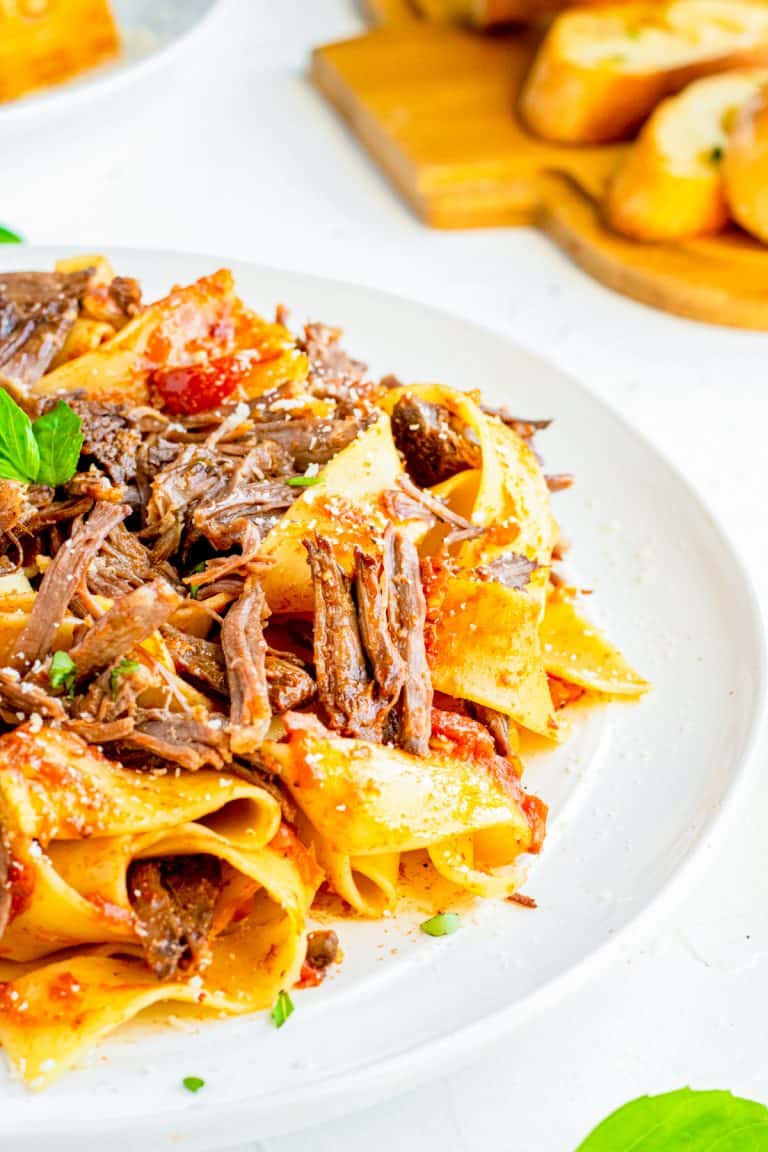 Braised beef short ribs shredded over pappardelle pasta on a white plate.