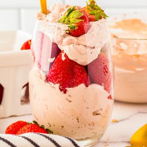 Square image of whipped cream in glass with strawberries.