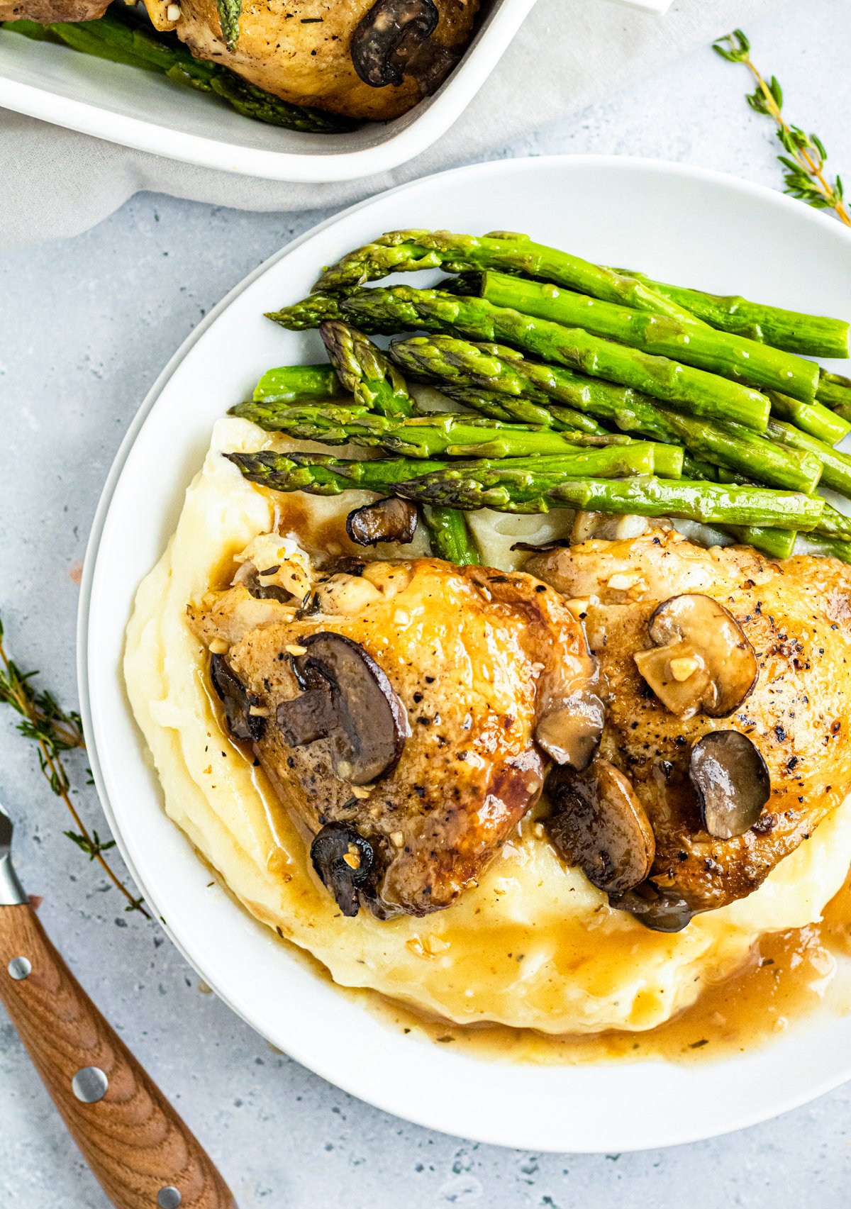 Overhead photos of Marsala Chicken Thighs over potatoes with asparagus