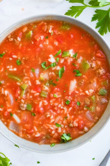 An overhead bowl of stuffed pepper soup with ground beef, rice, peppers, and tomatoes, garnished with parsley.