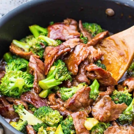 Beef and Broccoli in pan with bowl of rice in background.
