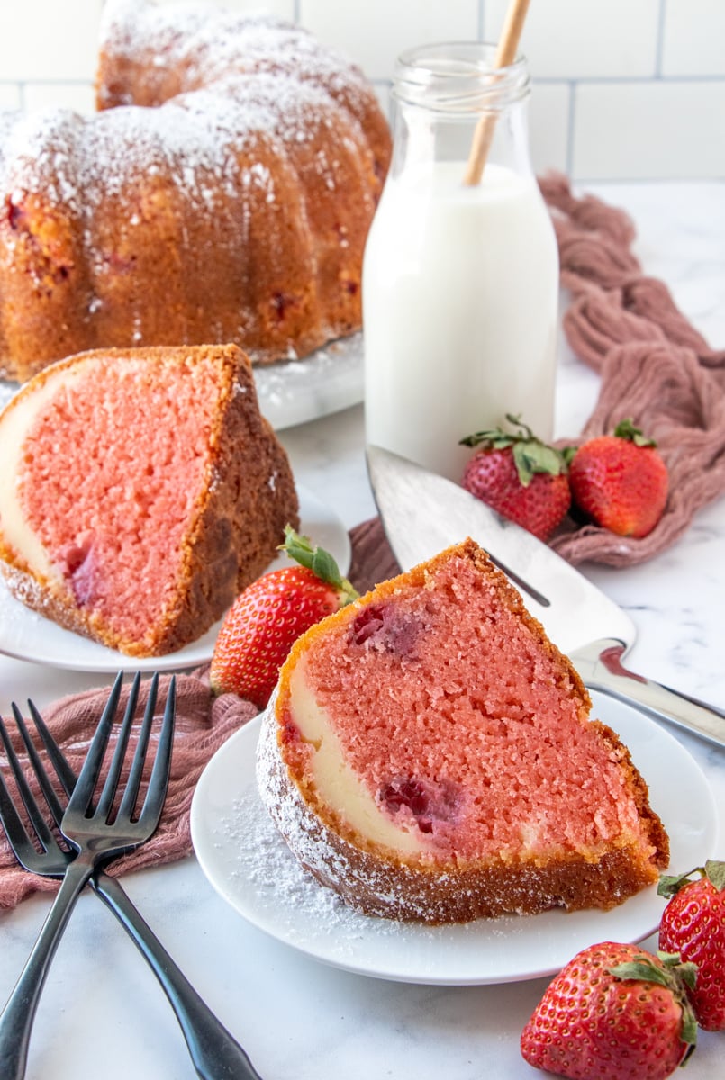 Slices of Strawberry Cheesecake Bundt Cake on two white plate with whole cake in background