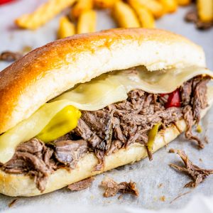 A slow cooker Italian beef sandwich on a hoagie roll with melty cheese, giardiniera, and pepperoncini.