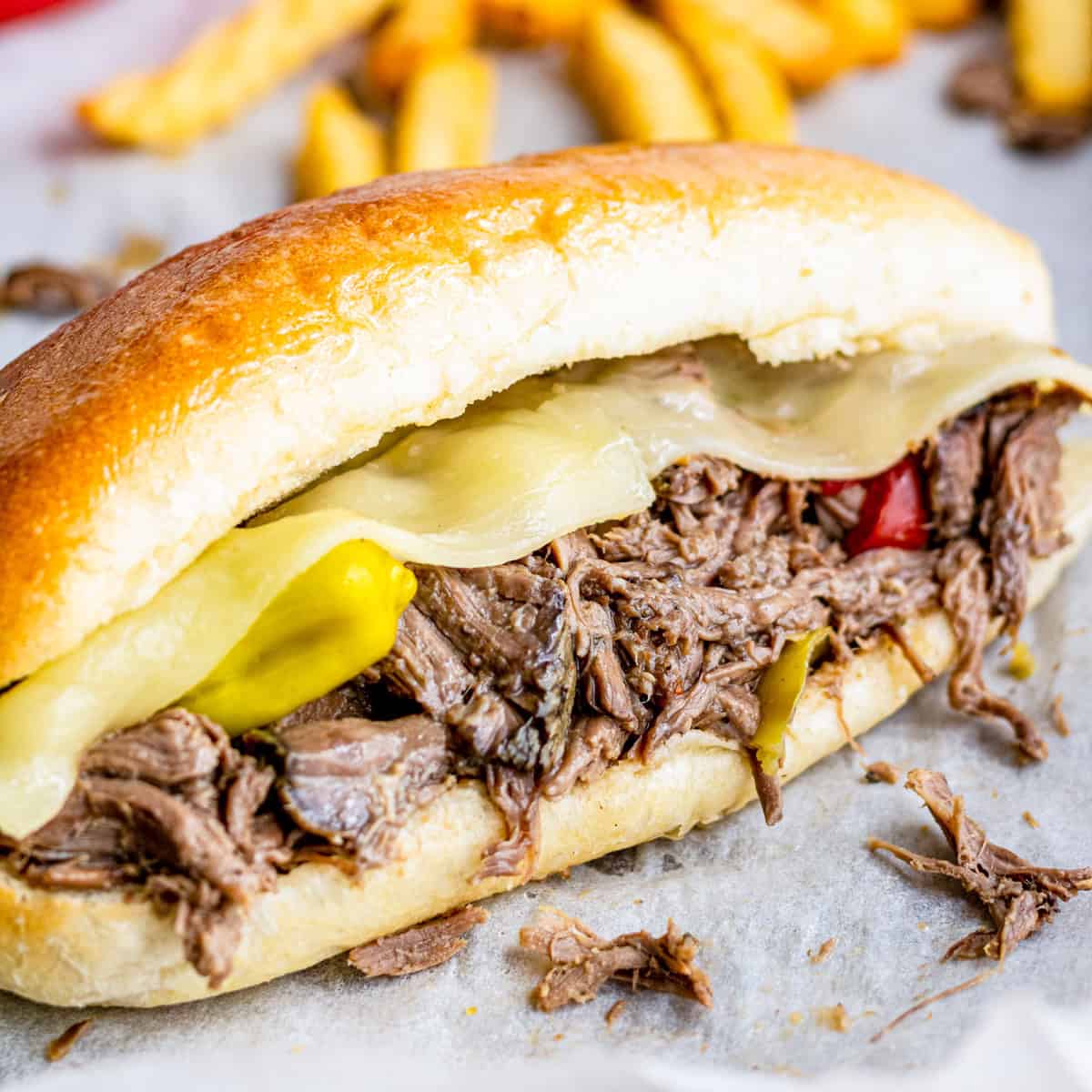 A slow cooker Italian beef sandwich on a hoagie roll with melty cheese, giardiniera, and pepperoncini.