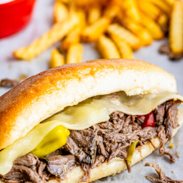 Close up of closed Slow Cooker Italian Beef Sandwich with French fries in background