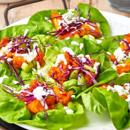 Finished Buffalo Chicken Lettuce Wraps with garnishes on white plate.