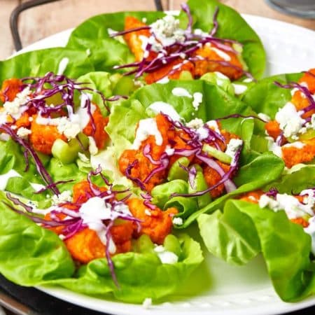 Finished Buffalo Chicken Lettuce Wraps with garnishes on white plate.