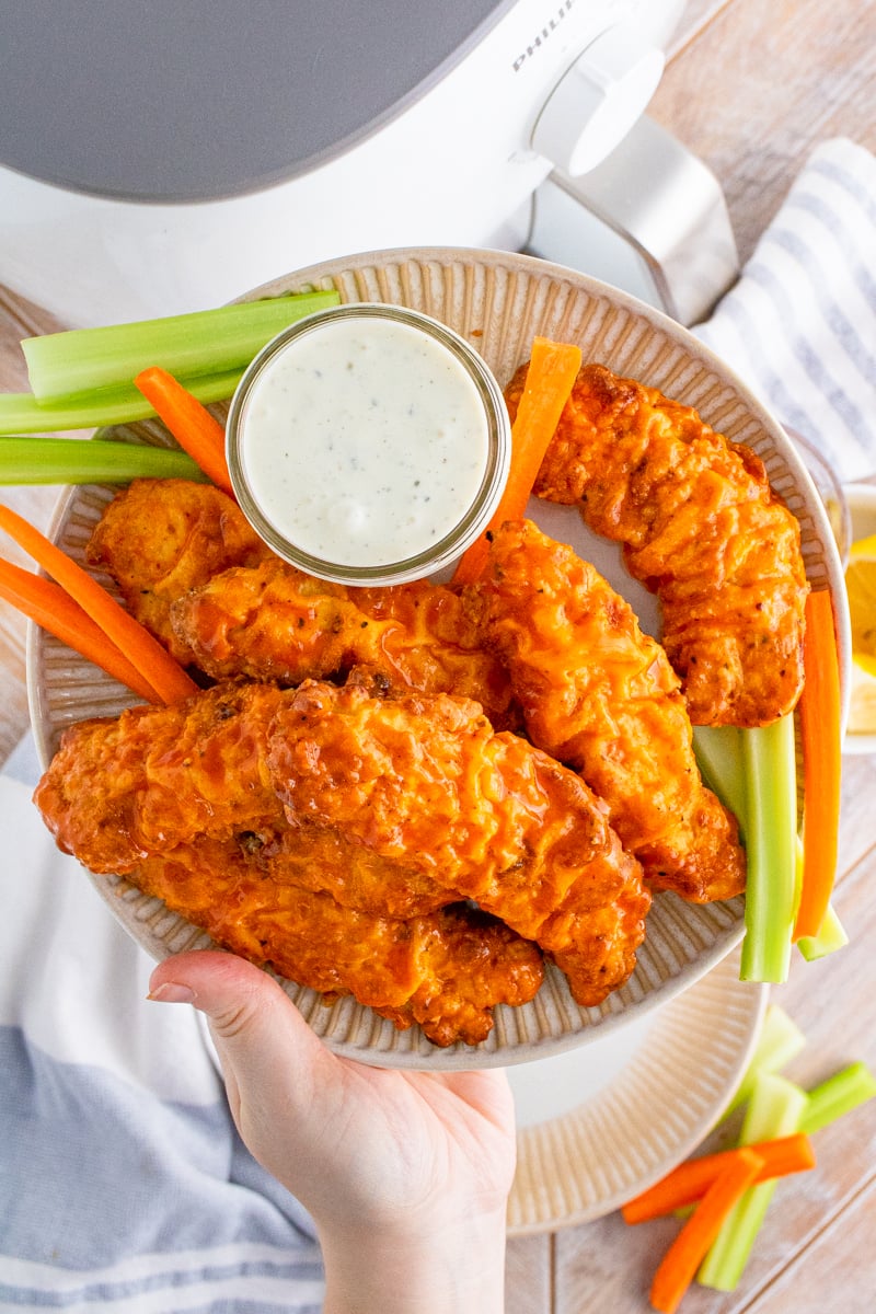 Hand holding up plate full of Buffalo Chicken Tenders