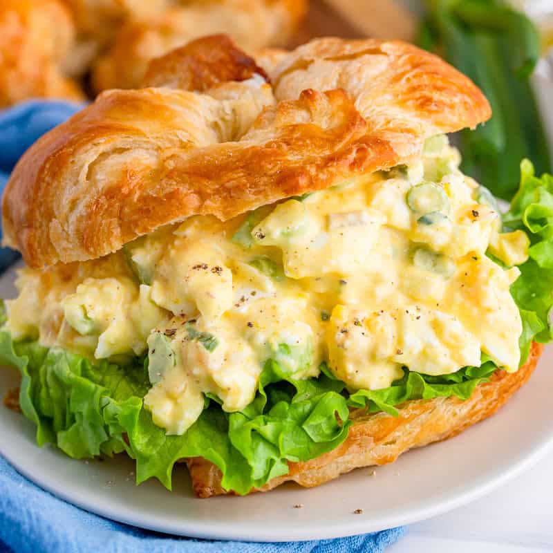 A creamy egg salad sandwich piled on a flaky croissant with lettuce.