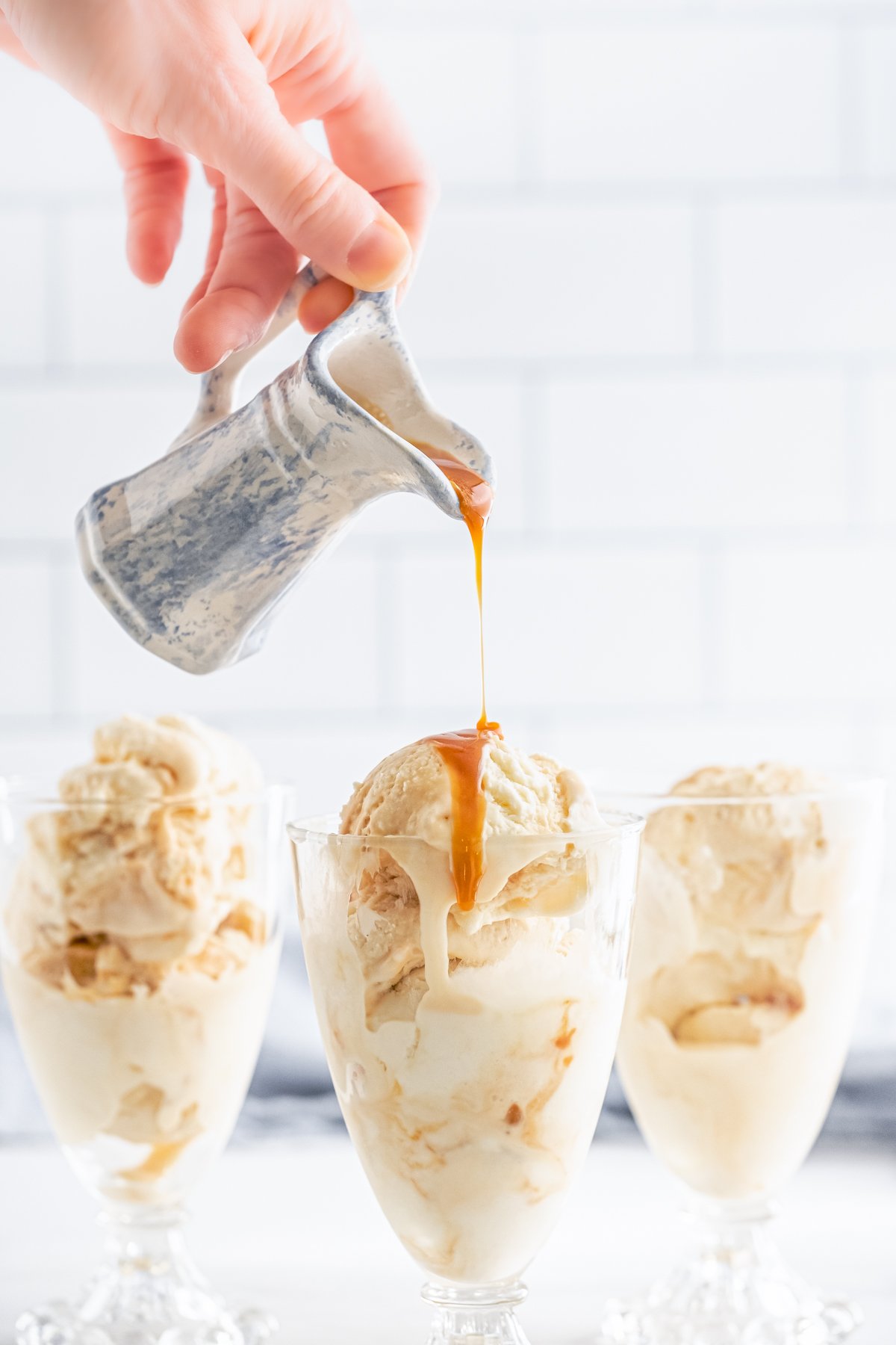 Caramel sauce being poured over on glass of ice cream