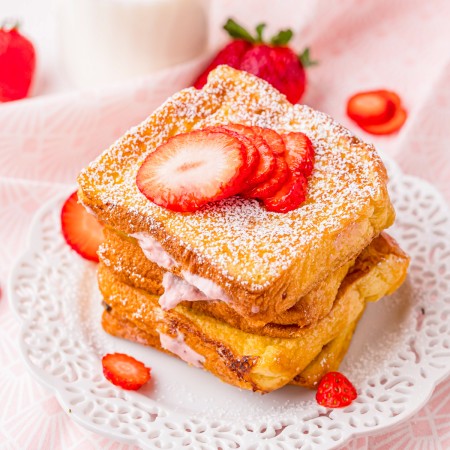 Square image of stacked French toast on white plate with strawberries