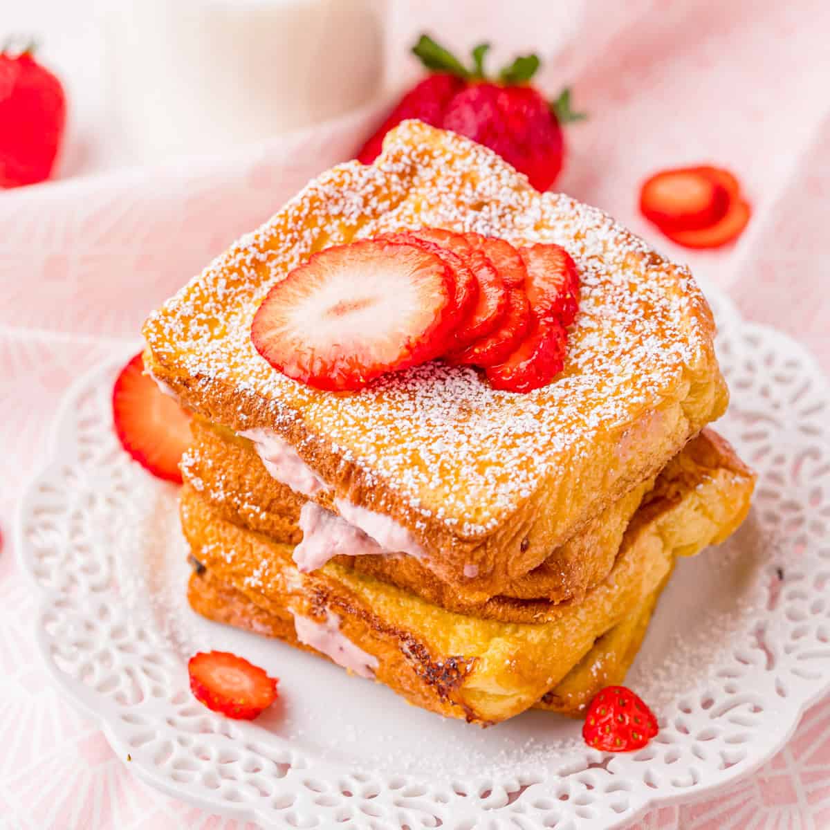 A stack of Strawberry Cheesecake Stuffed French Toast topped with sliced strawberries and powdered sugar.