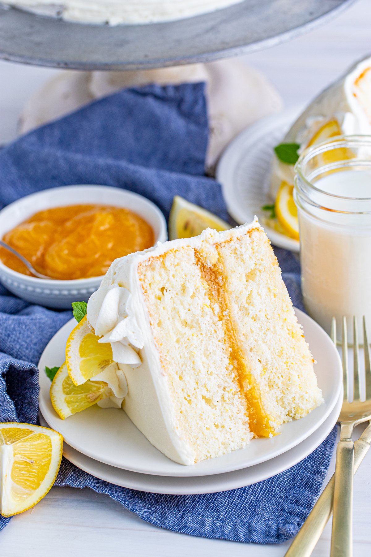 One slice of Lemon Layer Cake on white plate with lemon curd in background