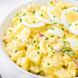 Square up close image of Classic Potato Salad in white bowl with hard-boiled eggs and chives for garnish