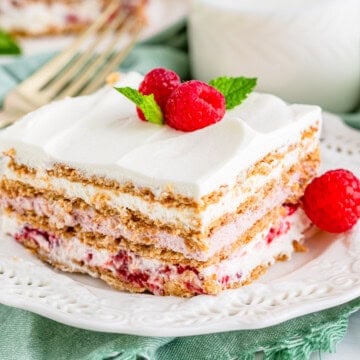 A slice of Raspberry Icebox Cake on a white plate topped with fresh raspberries and mint.