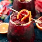 A red wine spritzer over ice garnished with an orange slice.
