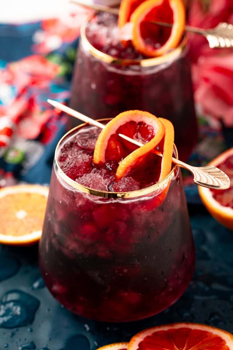 A red wine spritzer over ice garnished with an orange slice.