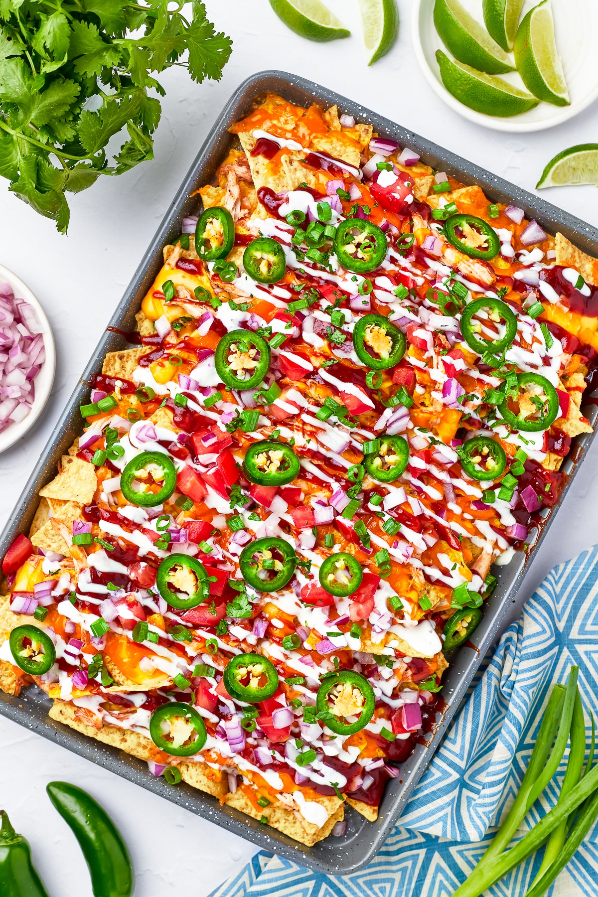 Overhead shot of BBQ Chicken Nachos on a sheet tray on a white background countertop and blue geometric linen