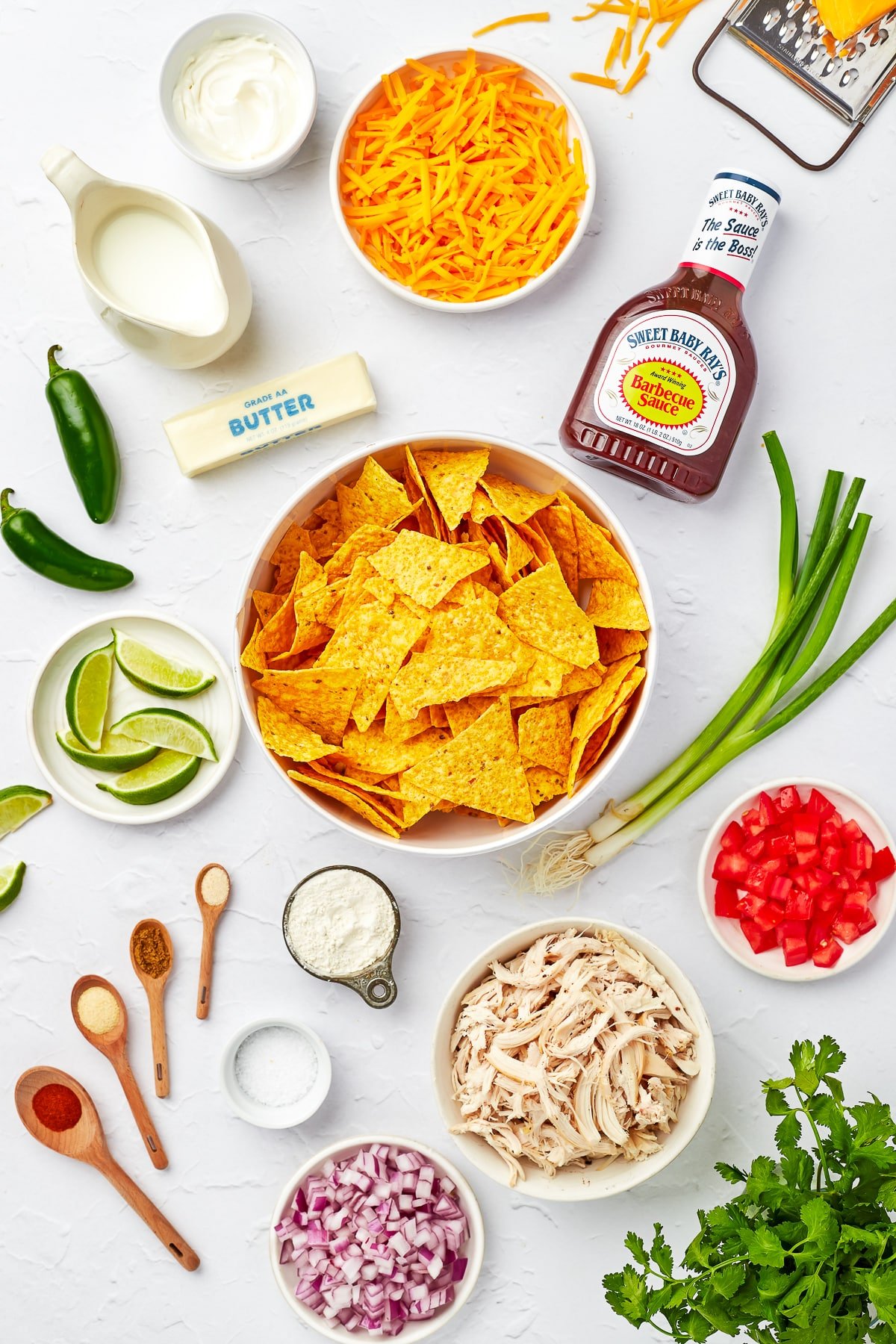 Overhead shot of the ingredients needed to make BBQ Chicken Nachos shown on a white stucco table top
