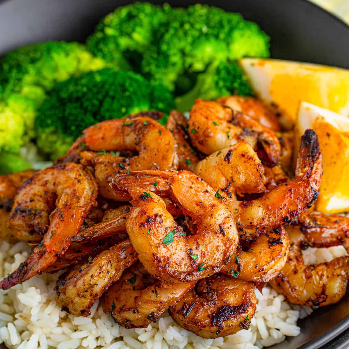 A plate of Blackened Shrimp served over rice with broccoli and lemon wedges.