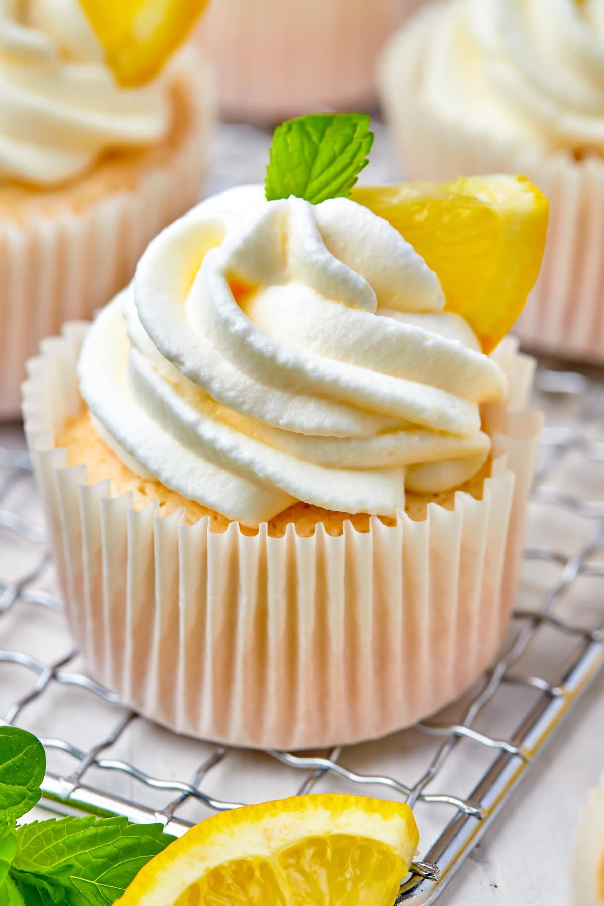 Upclose image of Angel Food Cupcake on a wire rack with lemon slices and sprig of mint