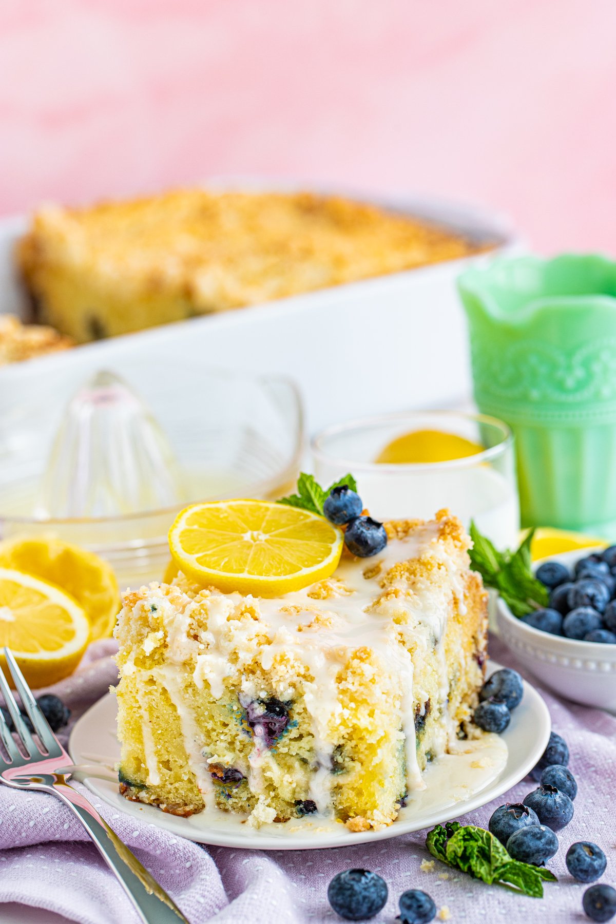 Slice of Lemon Blueberry Coffee cake on white plate topped with lemon, blueberries and mint