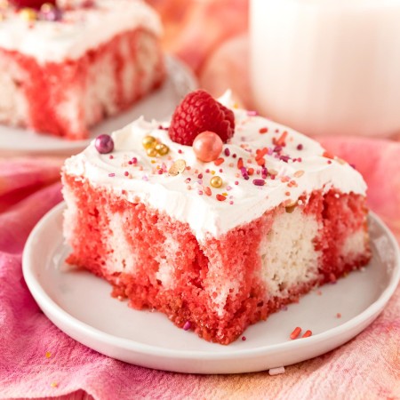 Square photo of Raspberry Jello Poke Cake decorated on white plate