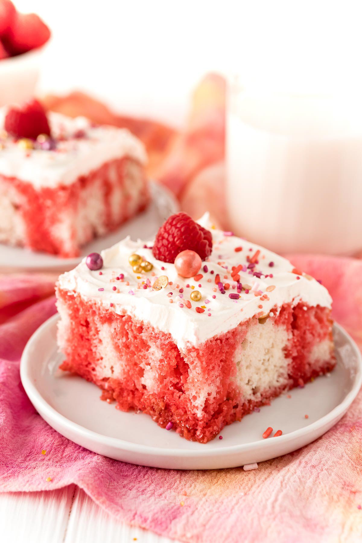 Slice of Raspberry Jello Poke Cake on white plate topped with sprinkles and raspberry