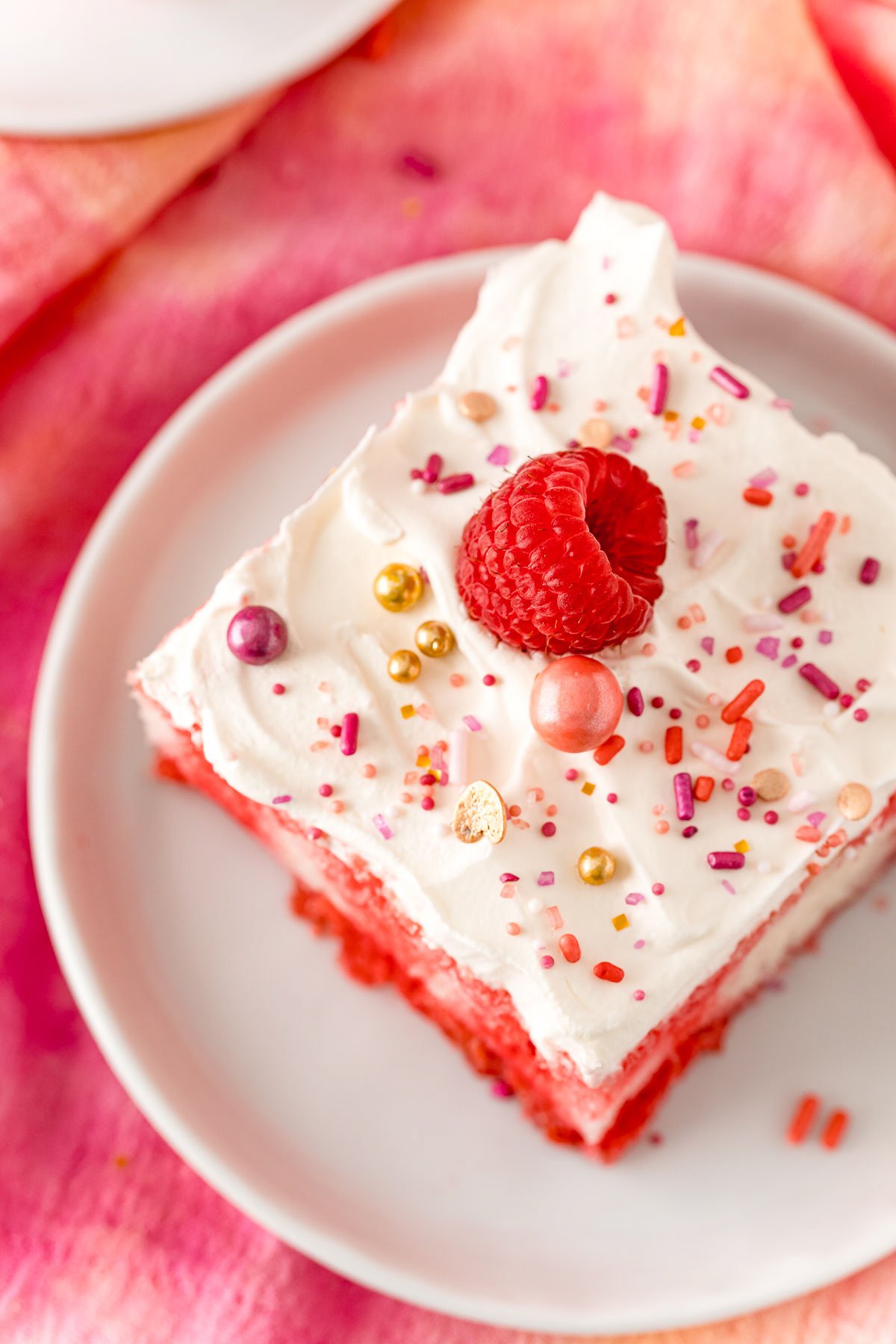Overhead of poke cake on white plate showing sprinkles and raspberry