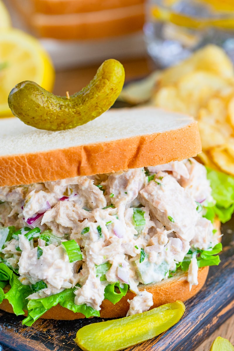 Close up of mixed up Tuna Salad Sandwich on bread topped with a pickle
