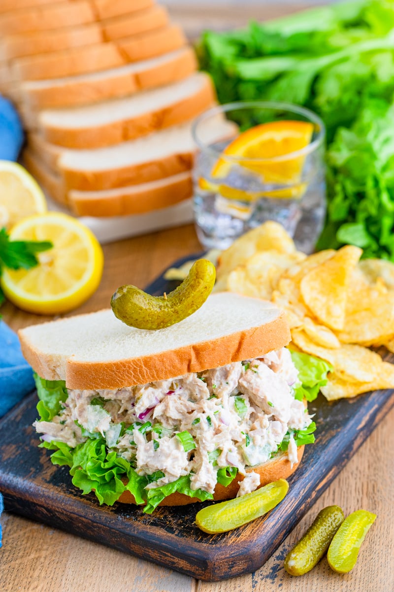 Finished Tuna Salad sandwich on wooden board with chips and bread in background