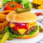 Square close up image of Cheeseburger Recipe on marble platter with onion rings and pickles