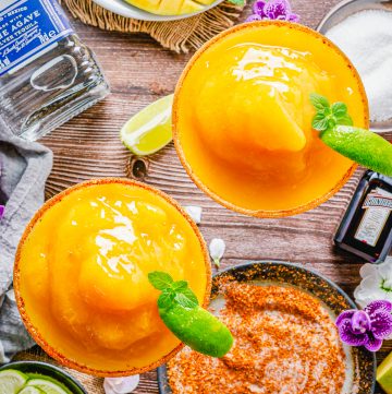 A frozen mango margarita with a chili lime salt rim and a lime wedge on a wooden board.