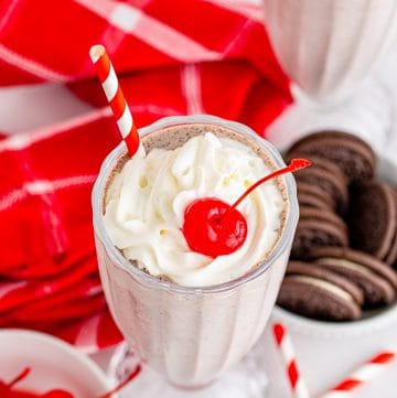 An Oreo Milkshake topped with whipped cream, cookie crumbs, and a cherry.