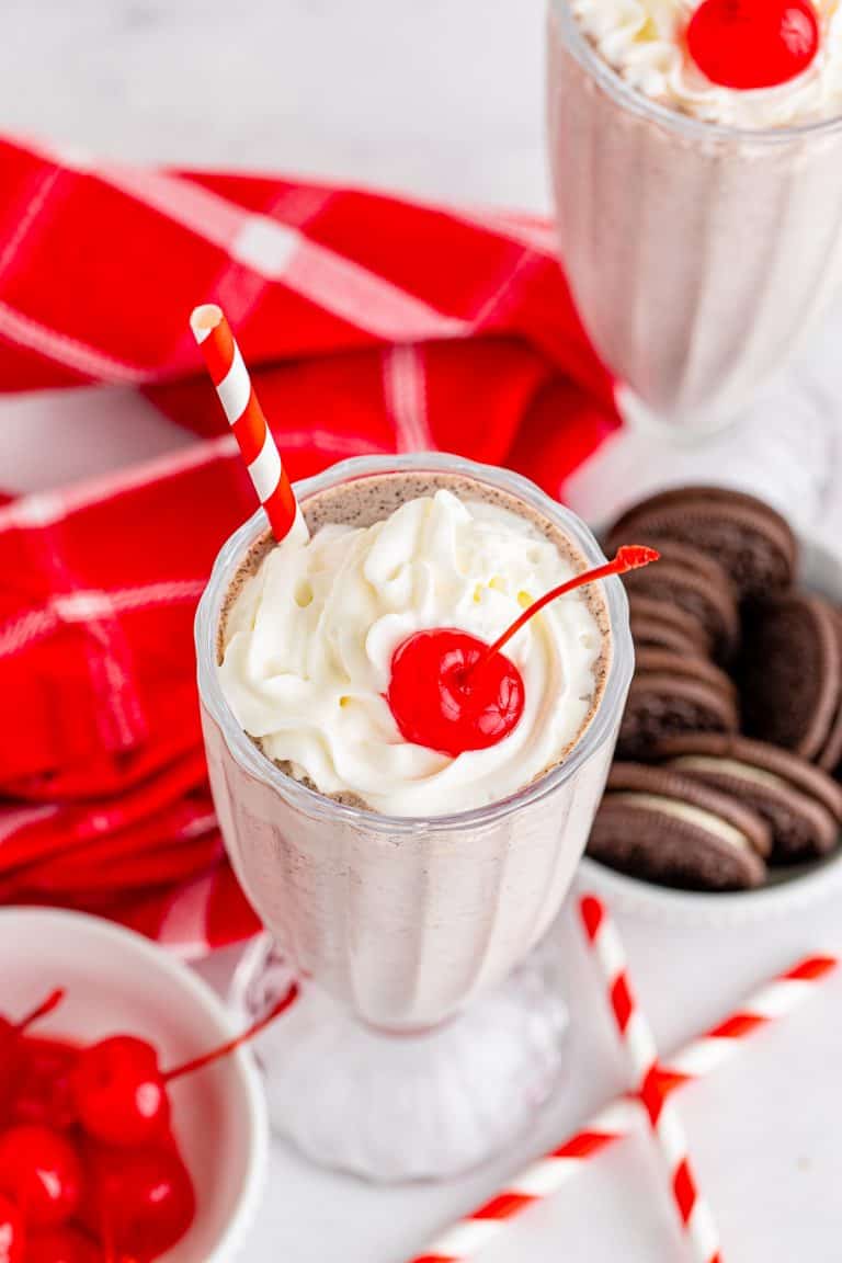 An Oreo Milkshake topped with whipped cream, cookie crumbs, and a cherry.