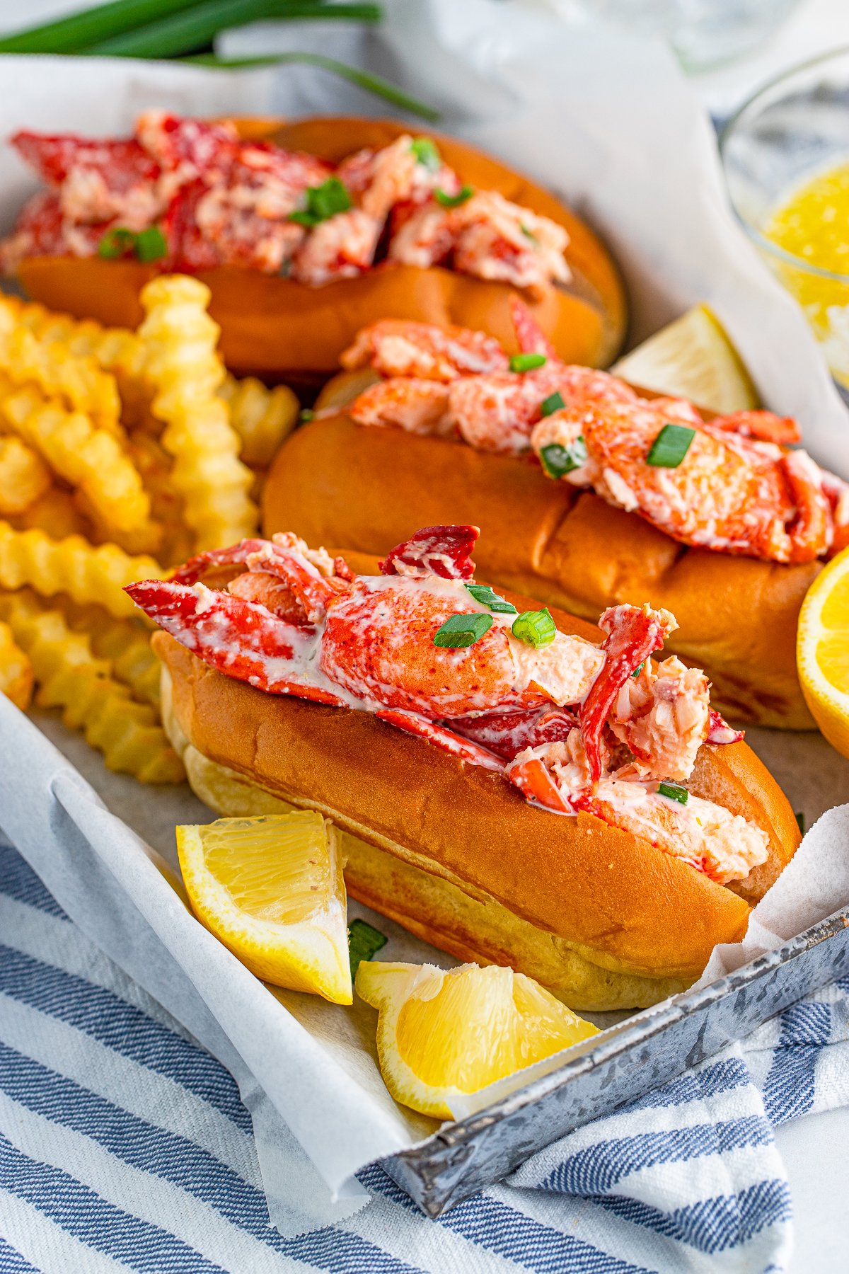 Three Lobster Rolls on tray with French fries and lemon wedges