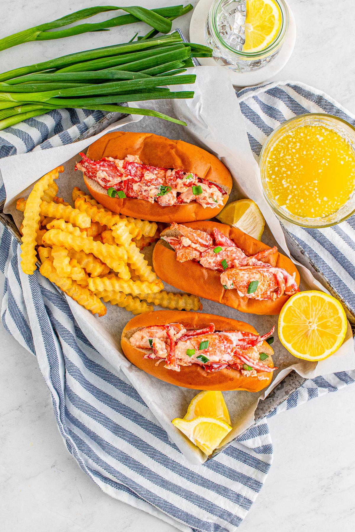 Overhead of Lobster Roll Recipe on tray with blue and white linen, fries, lemon and butter