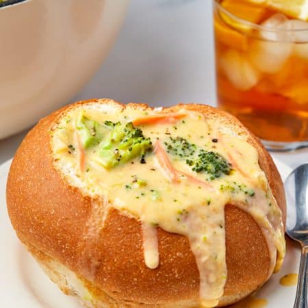 Bread bowl with Broccoli Cheddar Soup Recipe in it with drink and pot in background.
