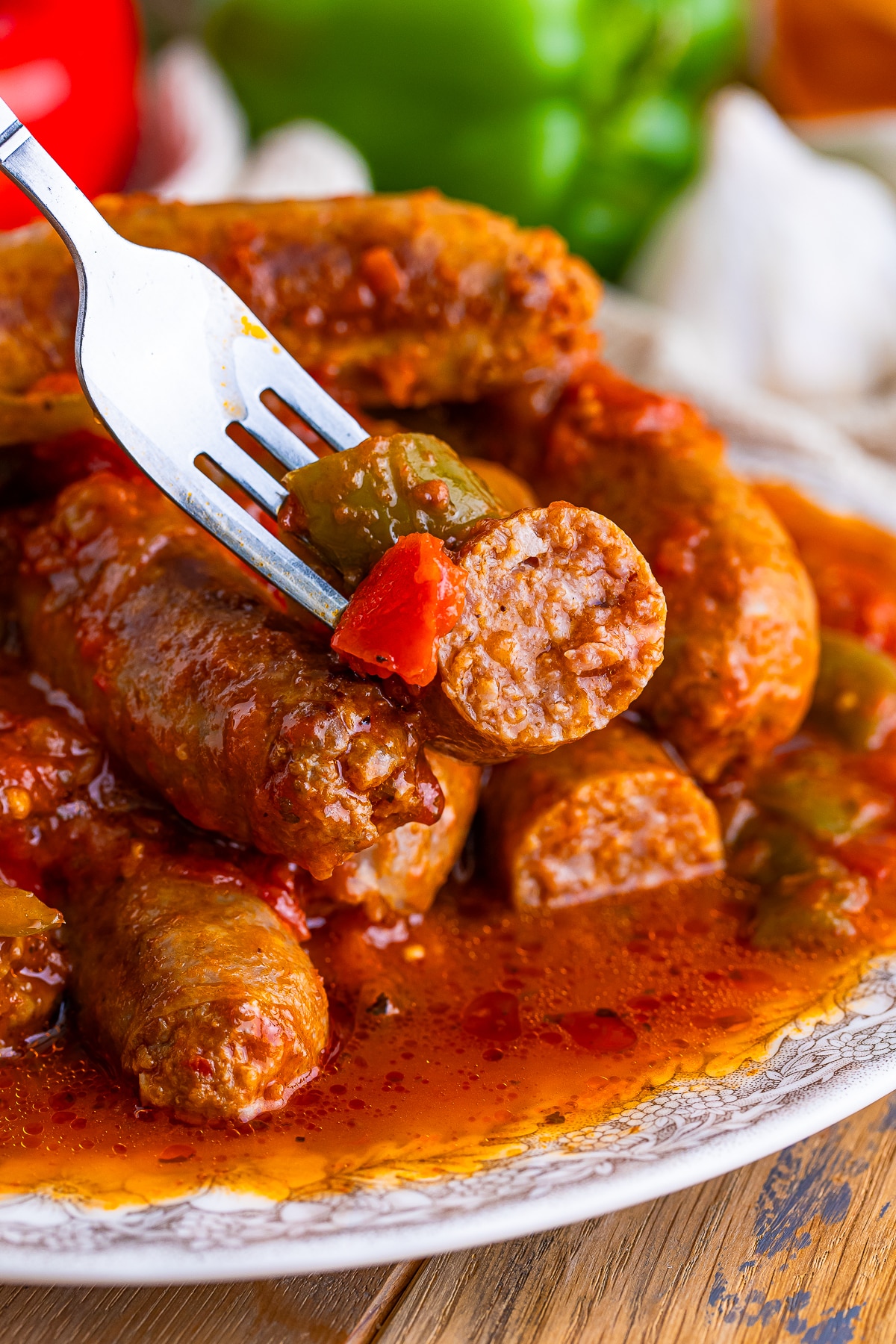 a fork holding up Italian Sausage and Peppers in air, sausage has been cut in half to show interior