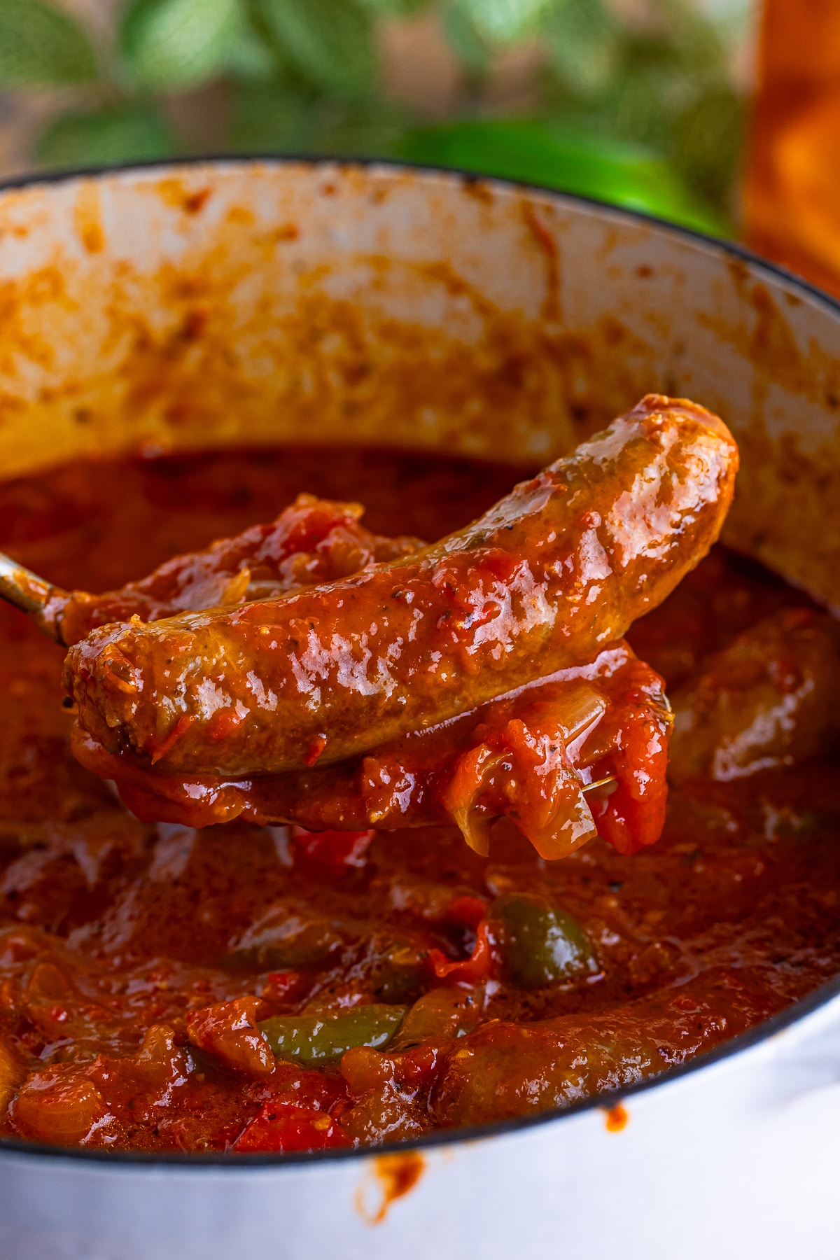 a spoon holding up Italian Sausage and Peppers in air over a pot