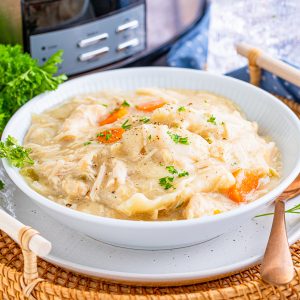 Square image of white bowl of Slow Cooker Chicken and Dumplings in front of slow cooker.