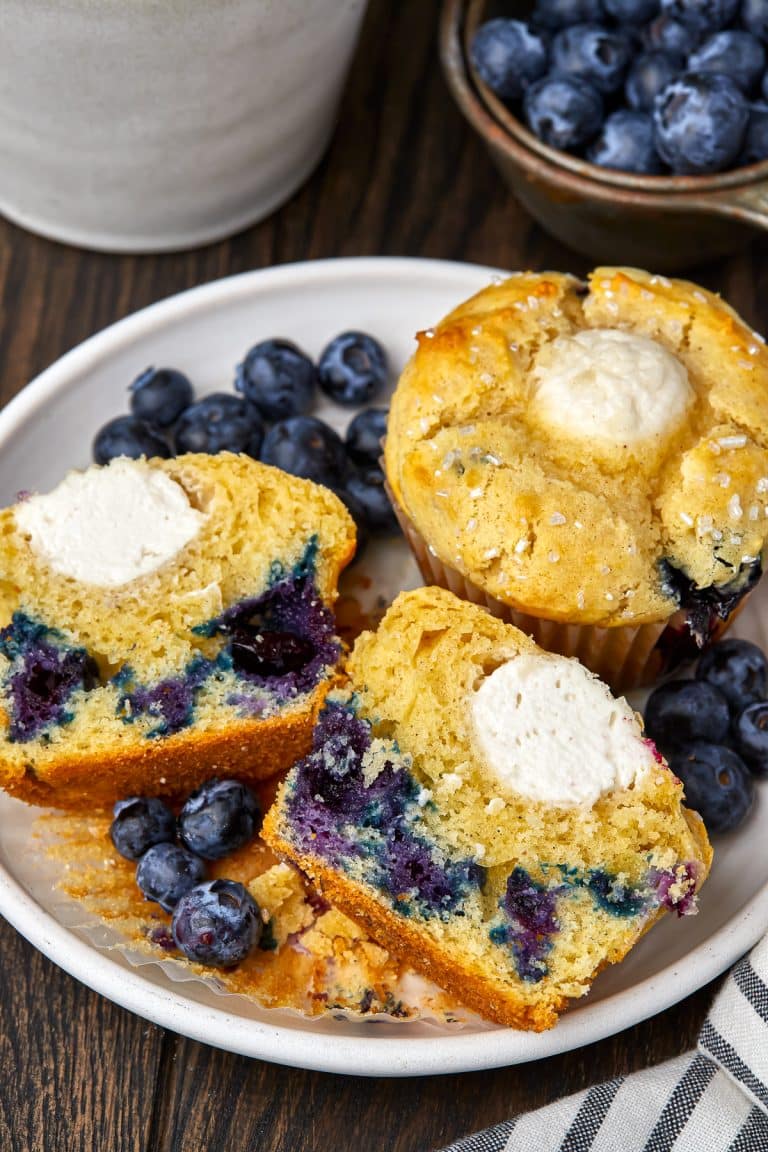 Blueberry muffins cut in half on a plate showing the creamy cream cheese center and juicy blueberries.