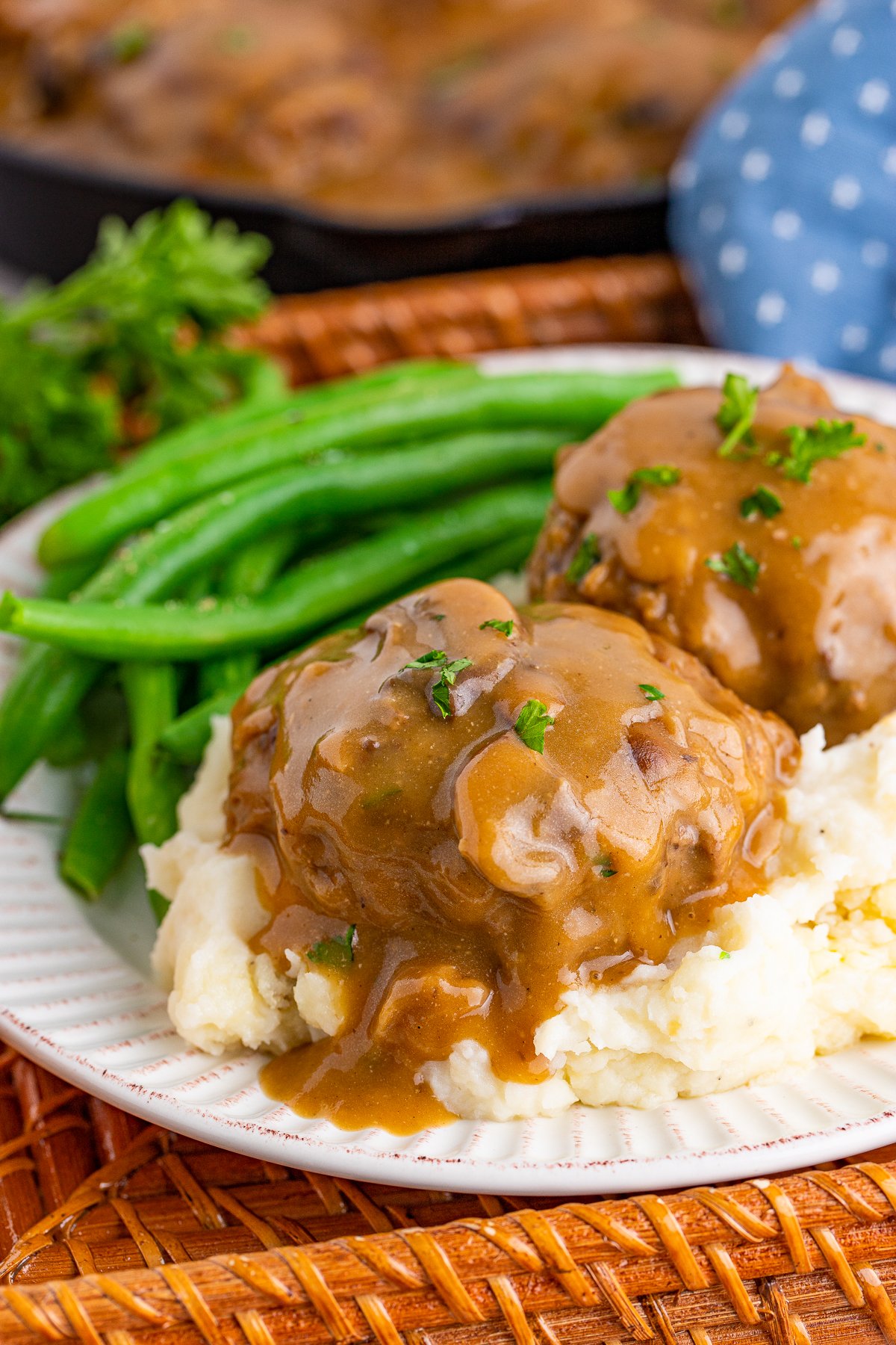 Salisbury Steak Recipe over potatoes with gravy and green beans on plate.