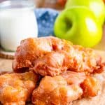 Three stacked Apple Fritter Recipe on parchment paper with apple and milk in background.