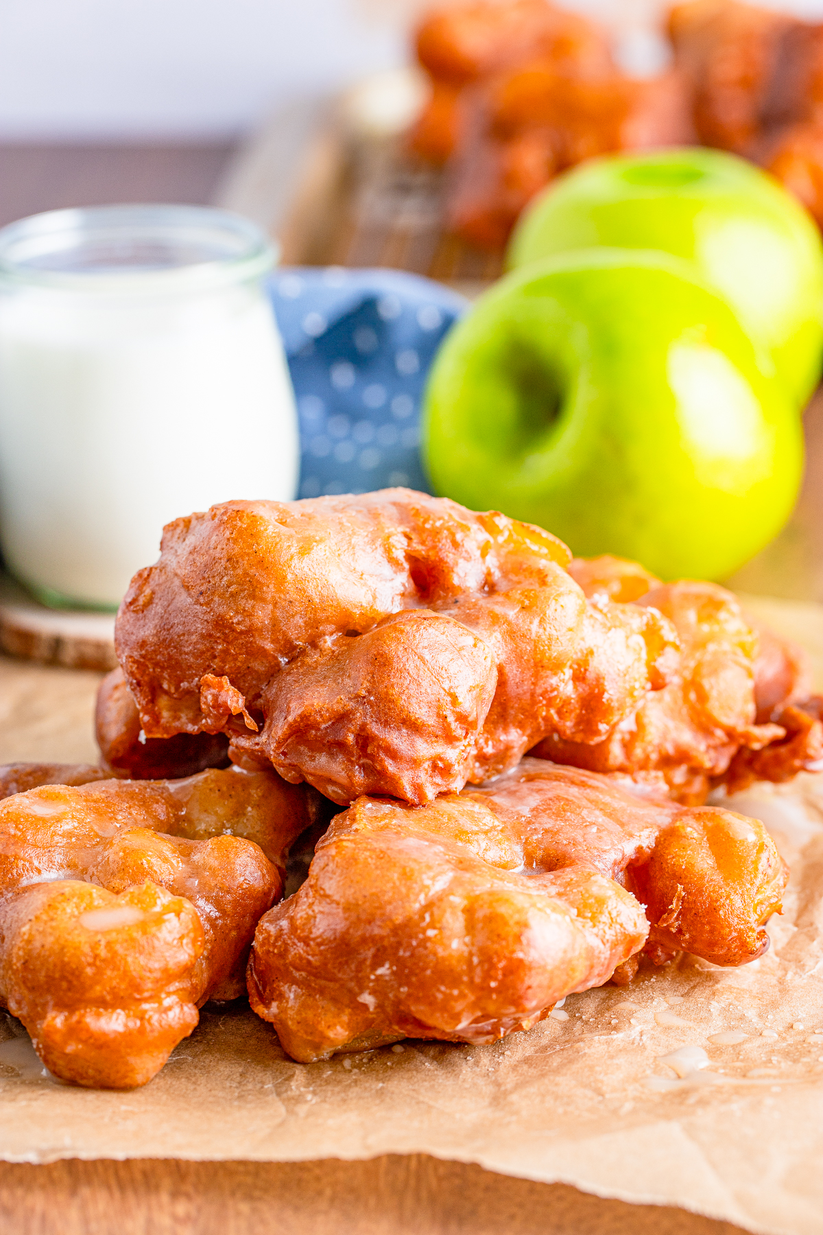 Three stacked Apple Fritter Recipe on parchment paper with apple and milk in background.
