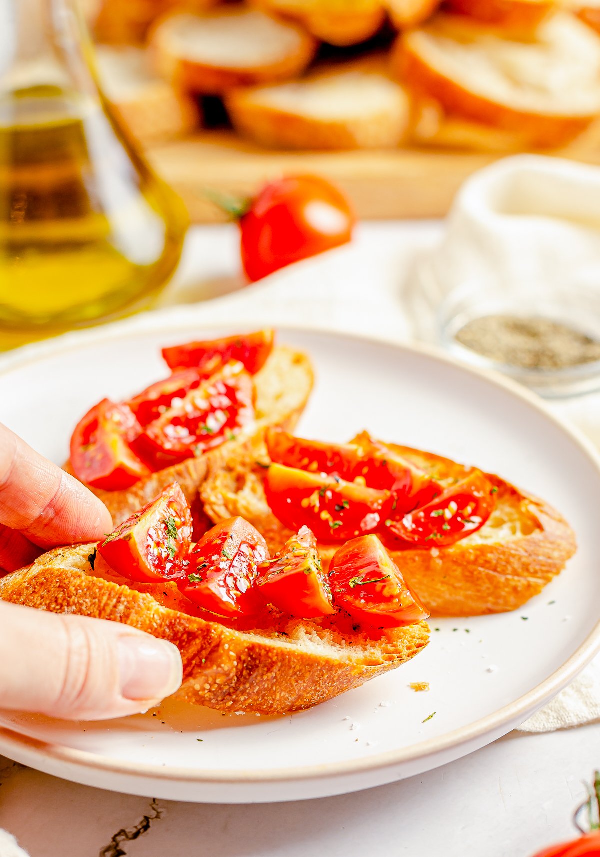 Hand putting a piece of Crostini Recipe on plate with tomatoes.