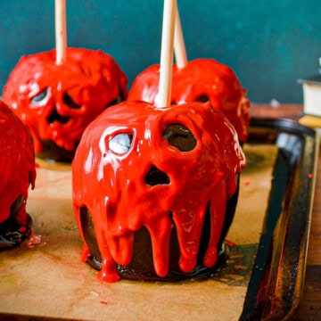 Poison apples with spooky red candy melt faces and black candy coating on a baking tray.