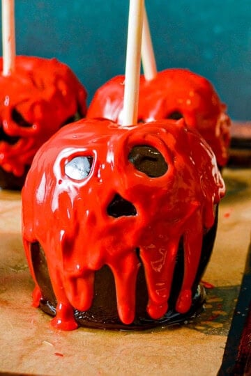 Poison apples with spooky red candy melt faces and black candy coating on a baking tray.