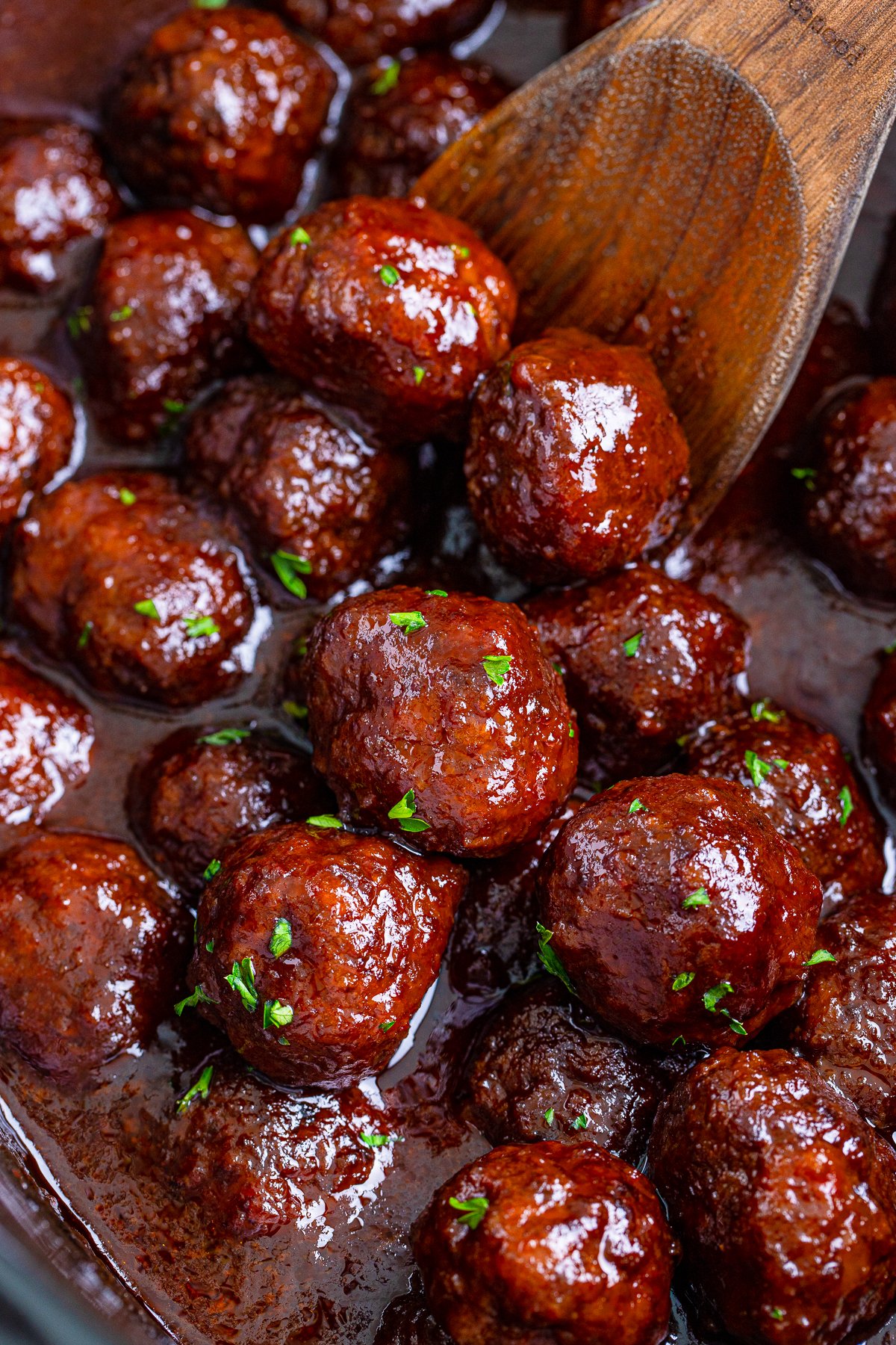 Close up of Grape Jelly Meatballs in Crock Pot with wooden spoon